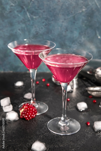 Glasses of Cosmopolitan cocktail with pomegranate and ice cubes on black table