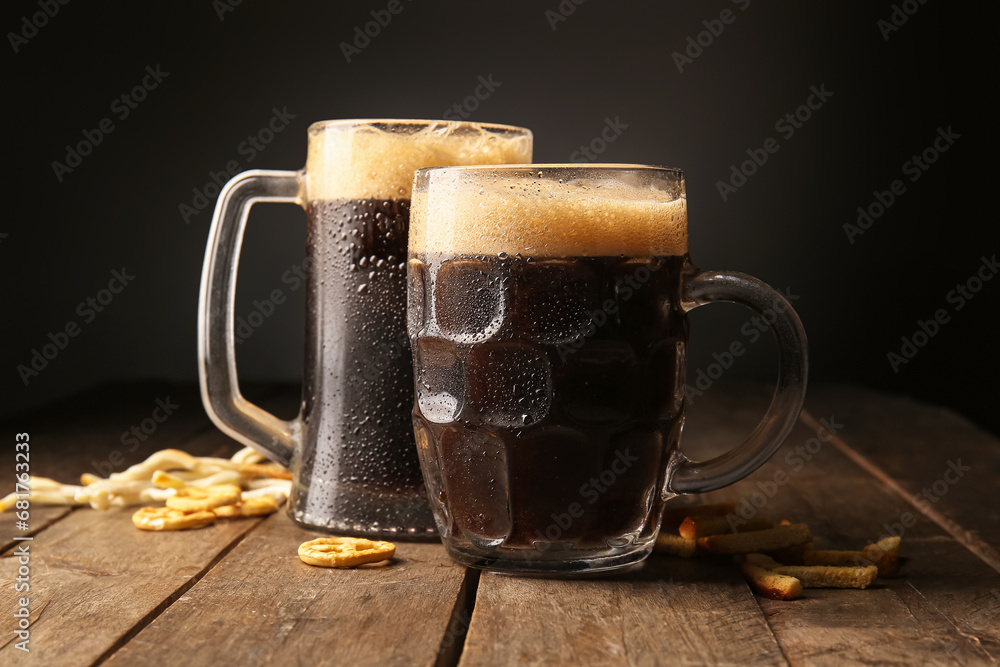 Mugs of dark beer and snacks on table against black background - obrazy, fototapety, plakaty 