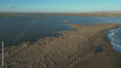 Fly over sandbank to reveal small flock of flamingoes standing in Orange River mouth estuary