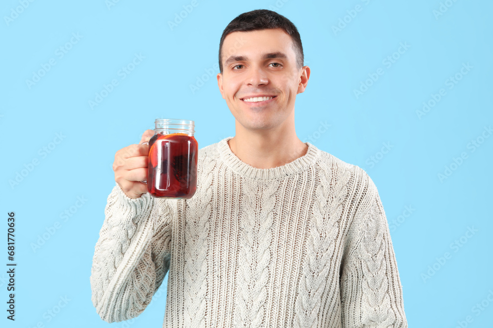 Handsome young man with glass of warm mulled wine on blue background Handsome young man with glass of warm mulled wine on blue background