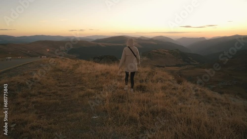 A beautiful Ukrainian young woman traveler walks along the high mountain in Romania Transalpina highway at sunset. Transalpina, Carpathian mountains in Romania at autumn sunrise photo