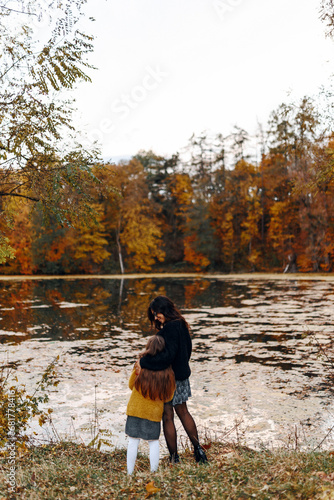 happy family: mother and child little daughter play hug on autumn nature walk by lake outdoors, have fun and smile, enjoy walk together, mother and daughter