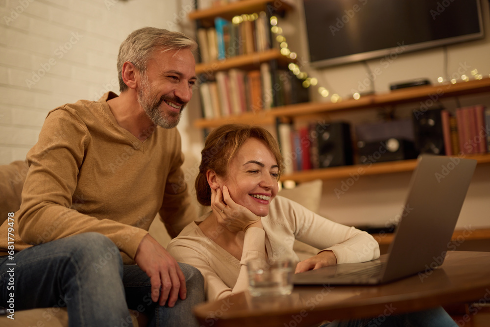 Happy mature couple enjoying their time together in the living room using laptop Happy mature couple enjoying their time together in the living room using laptop