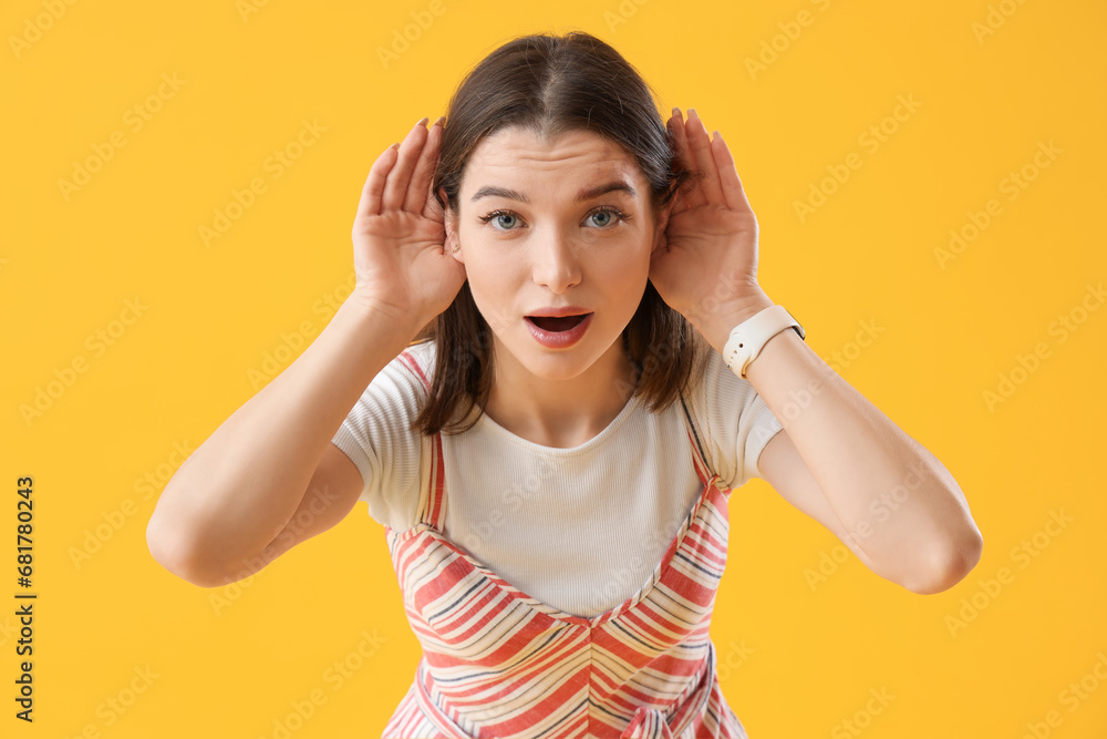 Young gossip woman trying to hear something on yellow background