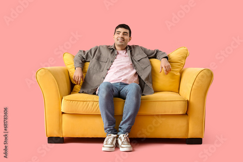 Handsome young man sitting on yellow sofa against pink background