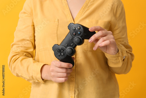 Young woman with game pad on yellow background, closeup