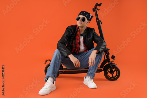 Cool young man with kick scooter on orange background