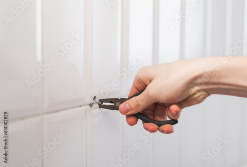 фотографія A young man pulls out a dowel from the wall using pliers.
