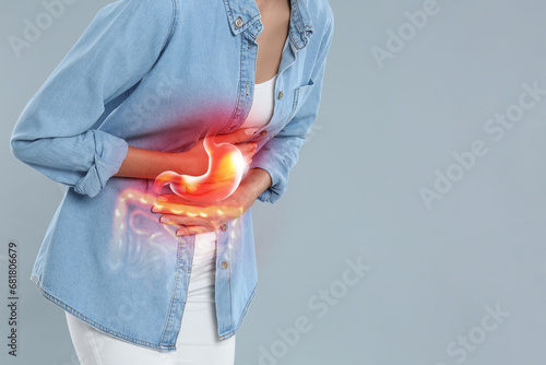 Woman suffering from stomach ache on grey background, closeup with space for text. Illustration of unhealthy gastrointestinal tract photo