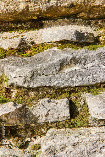 Grey stone wall with green moss, lichen growing between slabs of thick rock photo