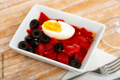 Traditional Spanish vegetable salad of baked red sweet peppers served with boiled egg garnished with olives photo