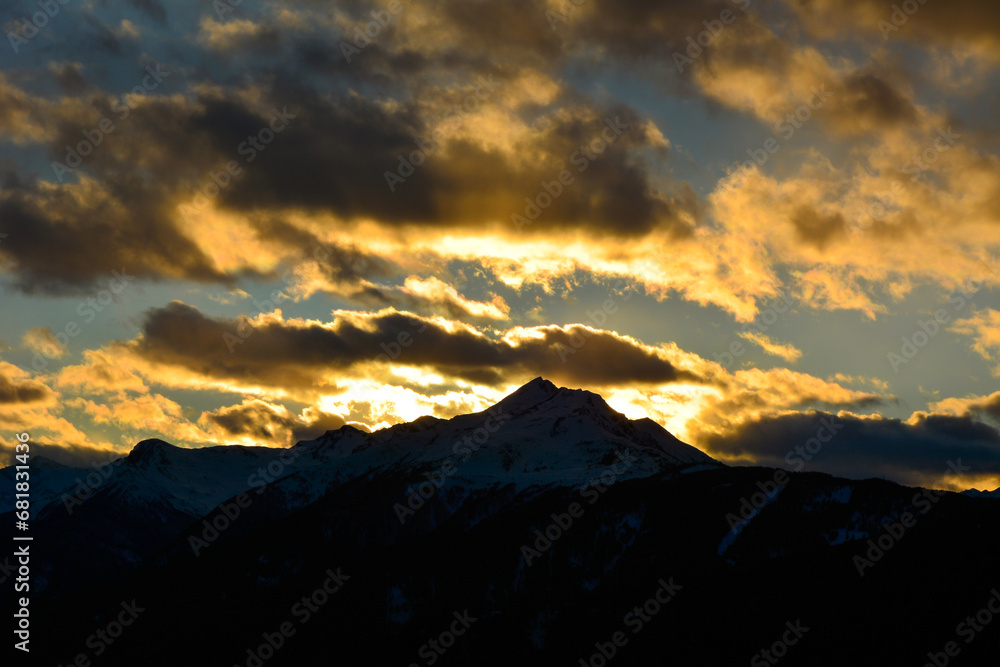 The evening sky with dark clouds against the background of the bright sun setting behind the mountains