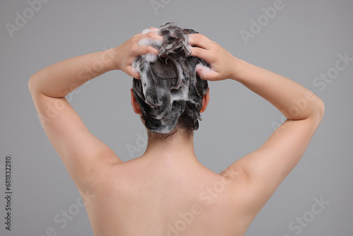 Woman washing hair on grey background, back view