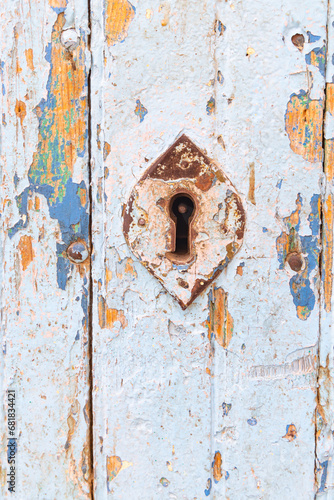 A keyhole on an old door with peeling paint.
