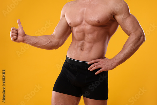 Young man is stylish black underwear showing thumb up on orange background, closeup