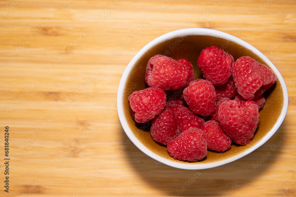 bowl with lots of fresh natural red raspberries, on light kitchen wooden board bowl with lots of fresh natural red raspberries, on light kitchen wooden board