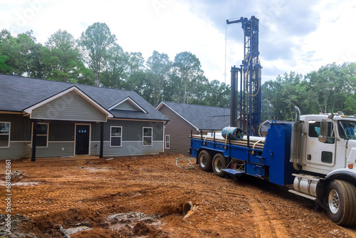 Using drilling machine workmen drill water well in suburban yard for artesian water.