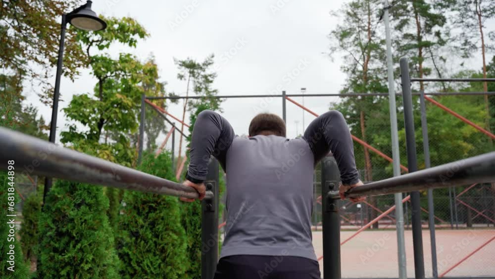 White Caucasian man trains on an outdoor sports field. Man doing gymnastics on parallel bars. Handsome man doing push-ups. Outdoor workout. Healthy lifestyle White Caucasian man trains on an outdoor sports field. Man doing gymnastics on parallel bars. Handsome man doing push-ups. Outdoor workout. Healthy lifestyle