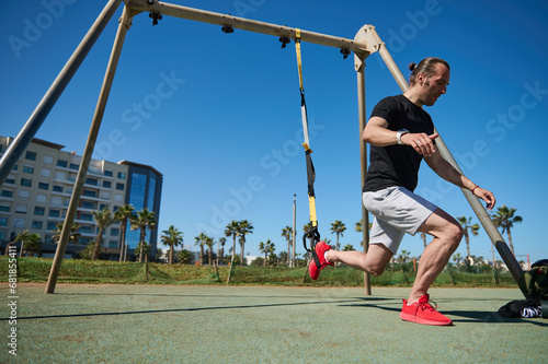 Muscular man performing lunges during exercise training workout bodyweight with suspension straps TRX.