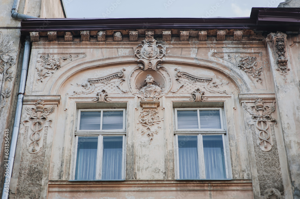 Windows with wooden frame. Neoclassical building of complex design with sandrik and mascarons in the form of a head sculpture. Light gray facade of an old house in Lviv, Ukraine.