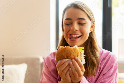 Hungry beautiful woman eating tasty American burger sitting in cafe