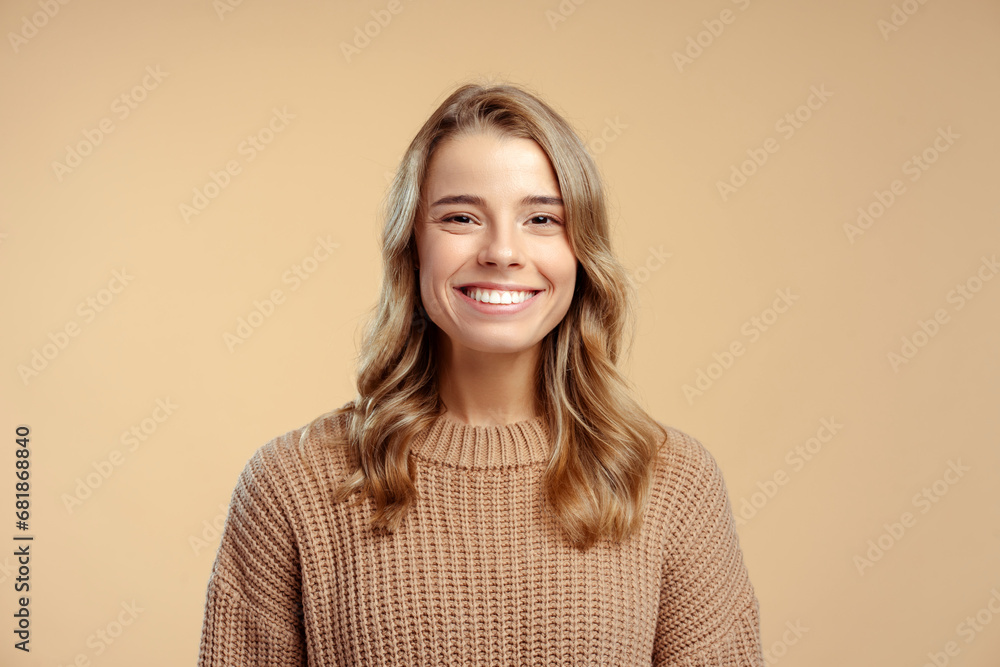 Portrait of smiling attractive young woman wearing stylish warm winter sweater looking at camera standing isolated on beige background. Concept of natural beauty - obrazy, fototapety, plakaty 