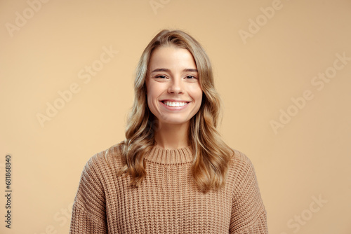 Portrait of smiling attractive young woman wearing stylish warm winter sweater looking at camera standing isolated on beige background. Concept of natural beauty