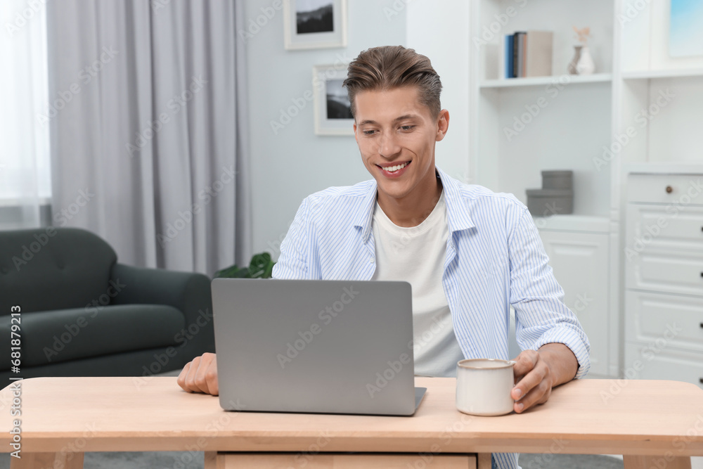Happy young man having video chat via laptop at wooden table indoors Happy young man having video chat via laptop at wooden table indoors