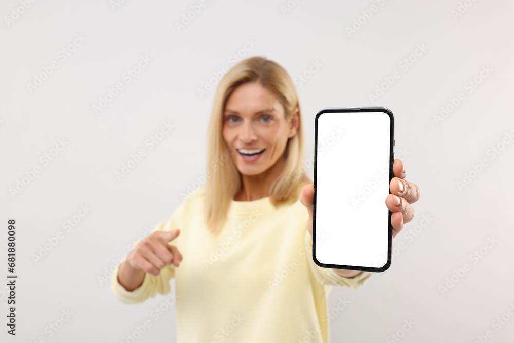 Happy woman holding smartphone and pointing at blank screen on white background, selective focus