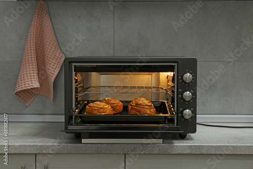 Open electric oven with delicious pastry on grey table in kitchen