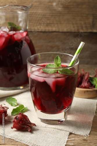 Glass of delicious iced hibiscus tea with straw and dry flowers on wooden table