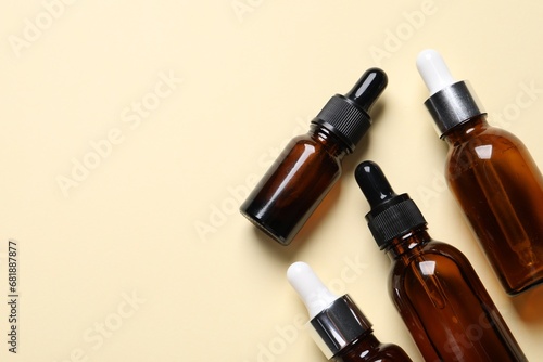 Many bottles with face serums on beige background, flat lay. Space for text