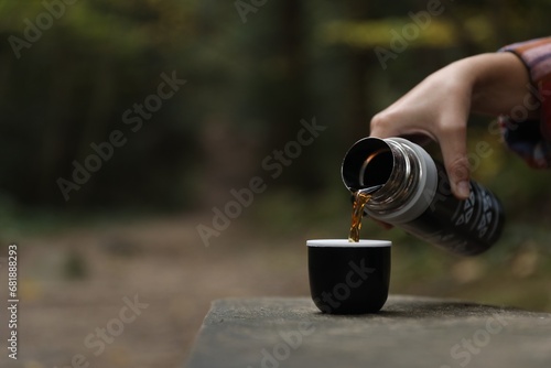 Woman pouring hot drink from black thermos into cup lid on bench outdoors, closeup. Space for text