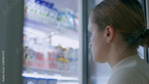 A woman with a tail chooses what to eat in the refrigerator, looks for something edible in the refrigerator and takes yogurt from the refrigerator. Profile of a young woman's face examines groceries