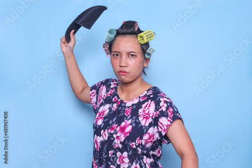 Angry Asian woman with hair curlers on head raise hand about to slap with sandal