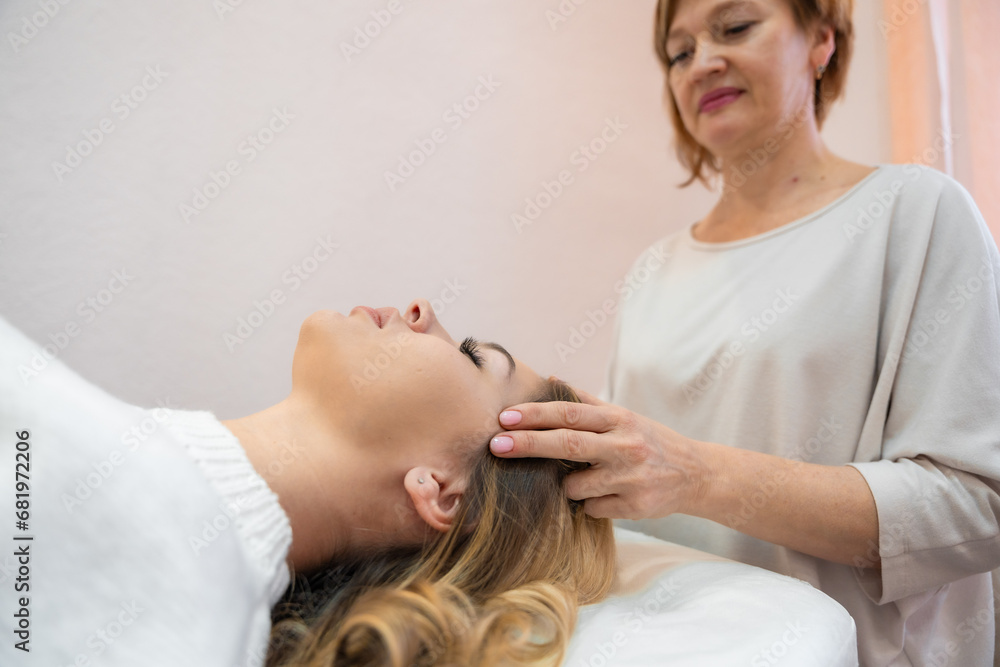 Healer performing by lightly touched set of 32 points of access bars on young woman head, stimulating positive change thoughts and emotions in salon. Alternative medicine concept