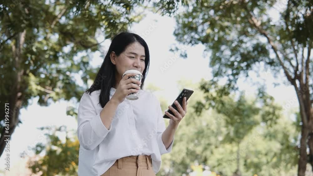 Young Asian woman using smartphone standing on a sunny day while drinking takeaway coffee in the park. Lifestyle and women concept. Young Asian woman using smartphone standing on a sunny day while drinking takeaway coffee in the park. Lifestyle and women concept.