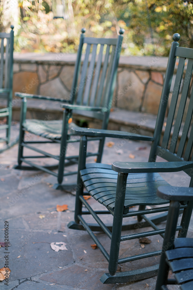 Green rocking chairs on a stone patio, a cozy and serene retreat amid fall foliage. Green rocking chairs on a stone patio, a cozy and serene retreat amid fall foliage.