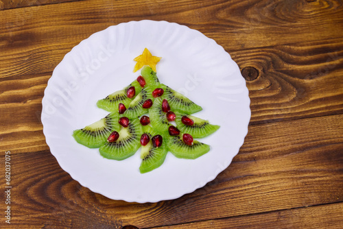 Christmas tree made of kiwi slices and pomegranate on wooden table. Top view. Creative idea for Christmas and New Year festive desserts. Funny food idea for kids