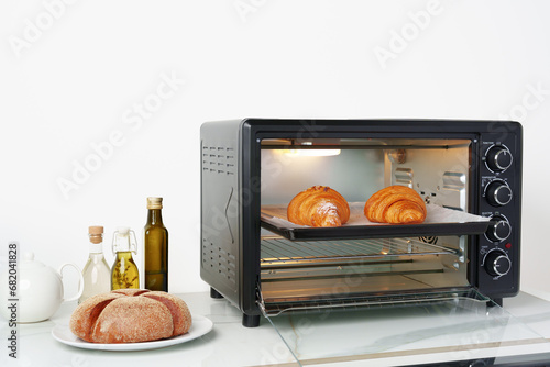 Modern mini electric oven with freshly baked croissants in kitchen