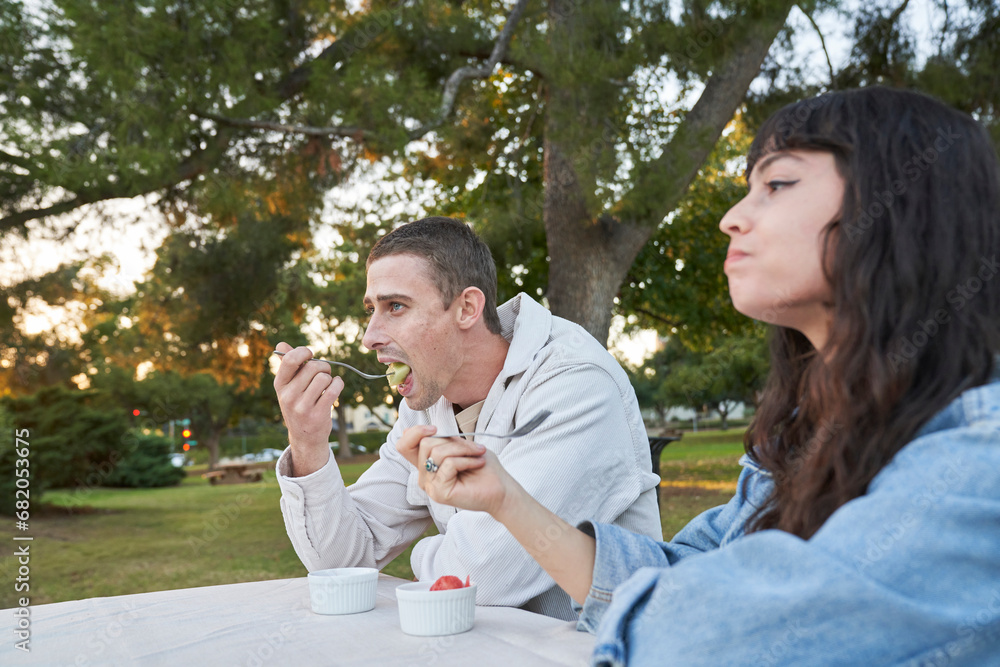 Fototapeta premium Couple eats fruit salad at picnic table in park