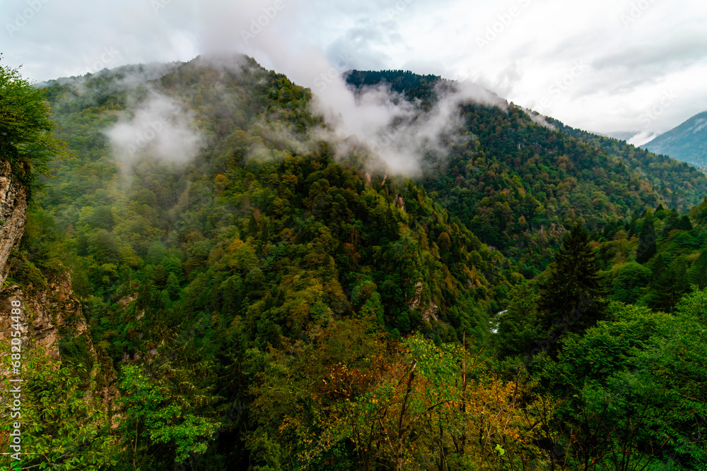 Foggy mountains in autumn. Aerial view of mountain slopes with yellow orange autumn trees in fog. Beautiful landscape with hills and misty forest.