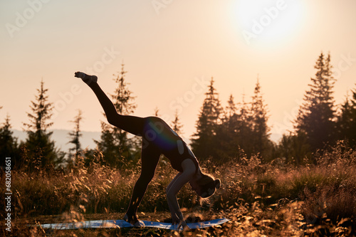 Attrective woman doing three legged dog pose. Sporty female workout in mountains at dawn. Meditating with view of sunrise photo