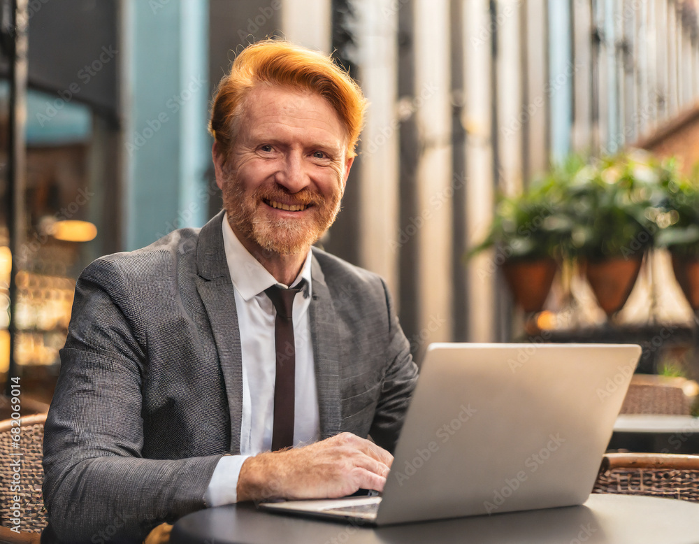 Stylish businessman in a suit working on laptop computer while sitting at a cafe outdoors Stylish businessman in a suit working on laptop computer while sitting at a cafe outdoors