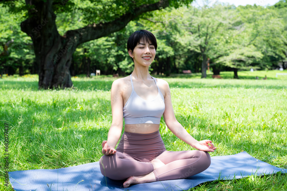 Beautiful Asian woman smiling and doing yoga in a beautiful grassy park. Urban living, wellbeing, mental health, happiness, environmental concern. Beautiful Asian woman smiling and doing yoga in a beautiful grassy park. Urban living, wellbeing, mental health, happiness, environmental concern.