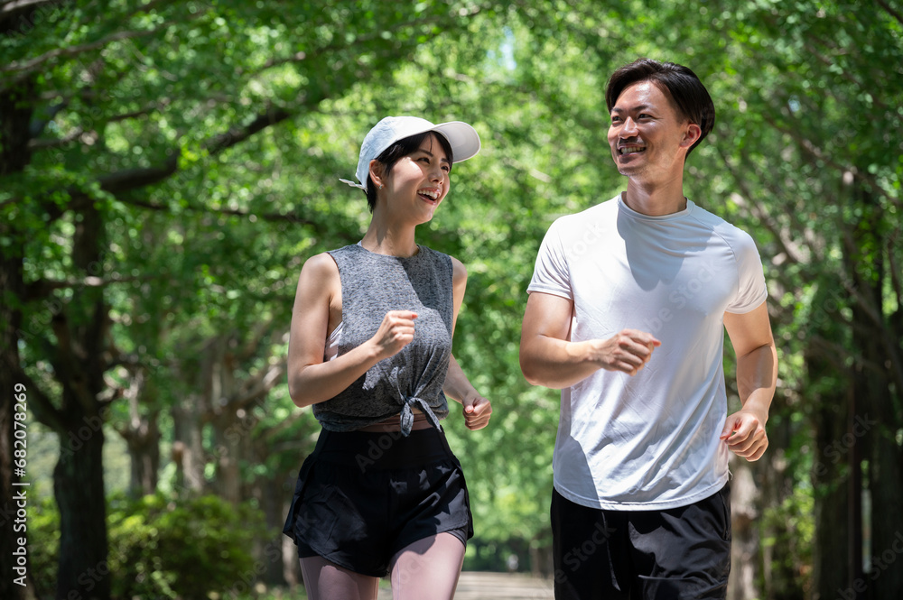 Fototapeta premium Young man and woman jogging along a tree-lined path in the park