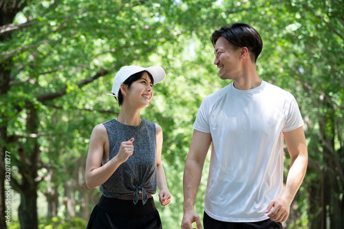 Young man and woman jogging along a tree-lined path in the park
