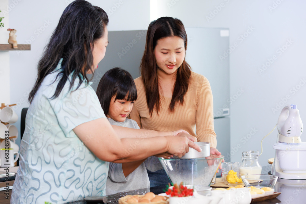 Asian female baker pastry chef mother and old senior grandmother helping teaching little girl daughter niece standing smiling holding using sieve sifting flour powder into glass bowl preparing dough Asian female baker pastry chef mother and old senior grandmother helping teaching little girl daughter niece standing smiling holding using sieve sifting flour powder into glass bowl preparing dough