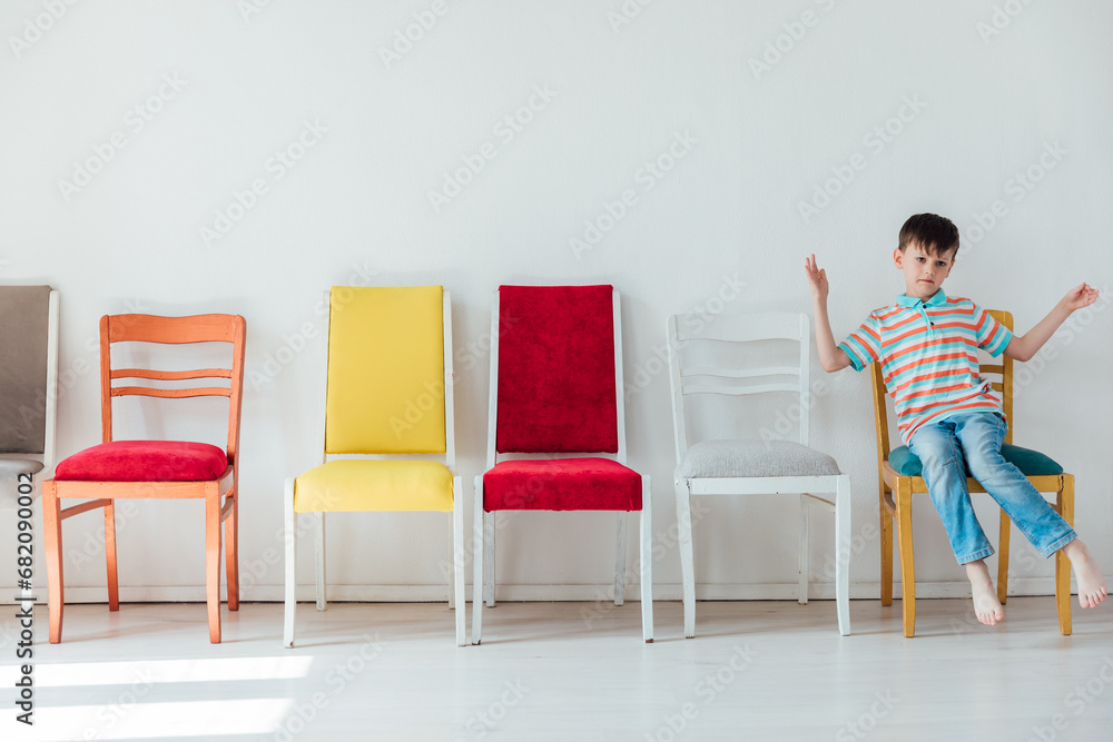 Fototapeta premium Cheerful little boy and many different colored chairs