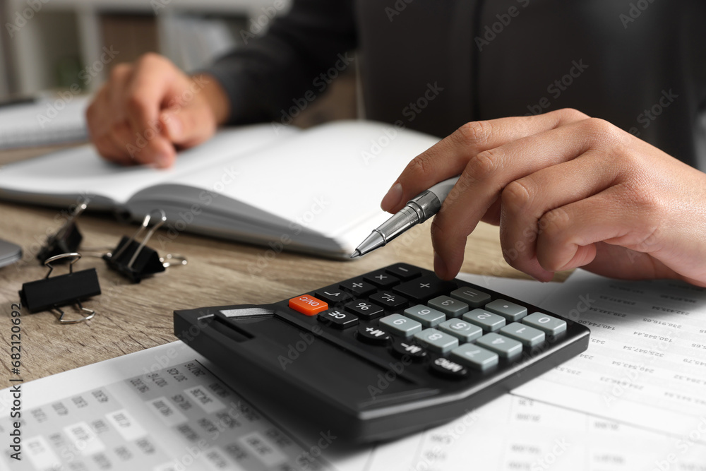 Woman using calculator at wooden table, closeup Woman using calculator at wooden table, closeup
